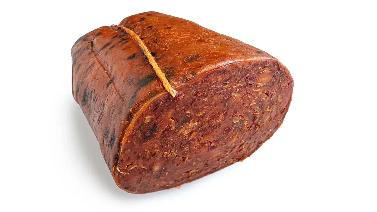 Ein Stück Nduja, eine kalabrische Streichwurst, mit grober Textur und roter Farbe, an einem Faden gebunden.
