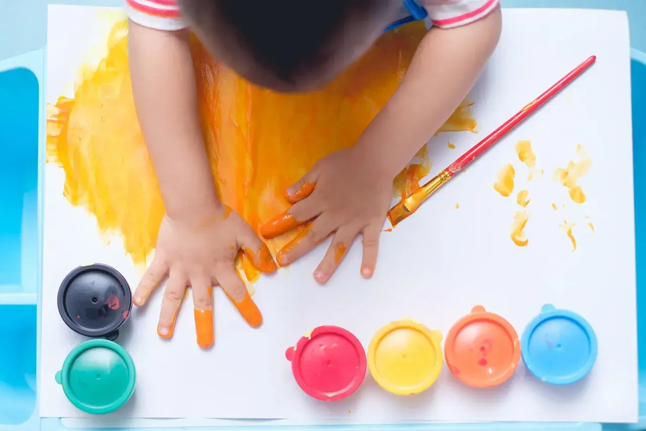 Manos pequeñas pintando con dedos y pincel. Un niño se divierte pintando con niños, rodeado de botes de pintura de colores.