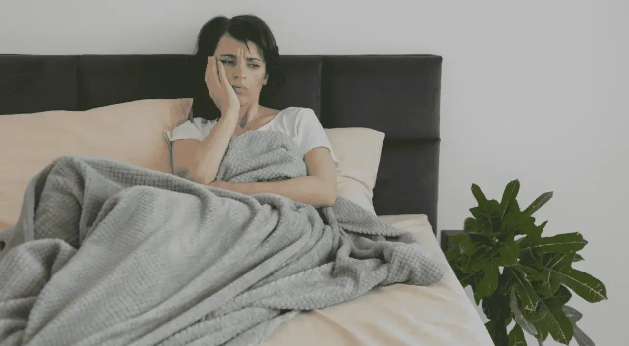 En kvinna ligger i sängen, med handen mot ansiktet. Det är svårt att vakna på morgonen adhd.