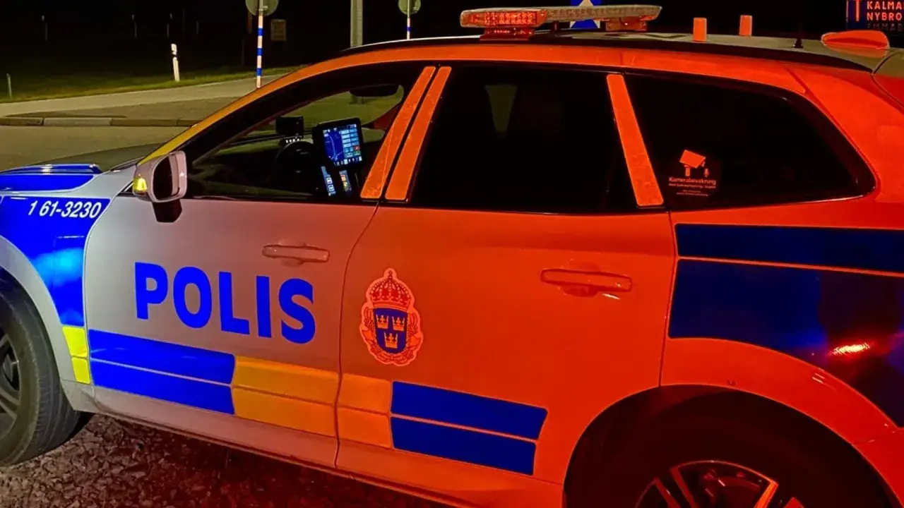 En polisbil med blåljus syns i mörkret. Texten "POLIS" är tydlig på sidan.