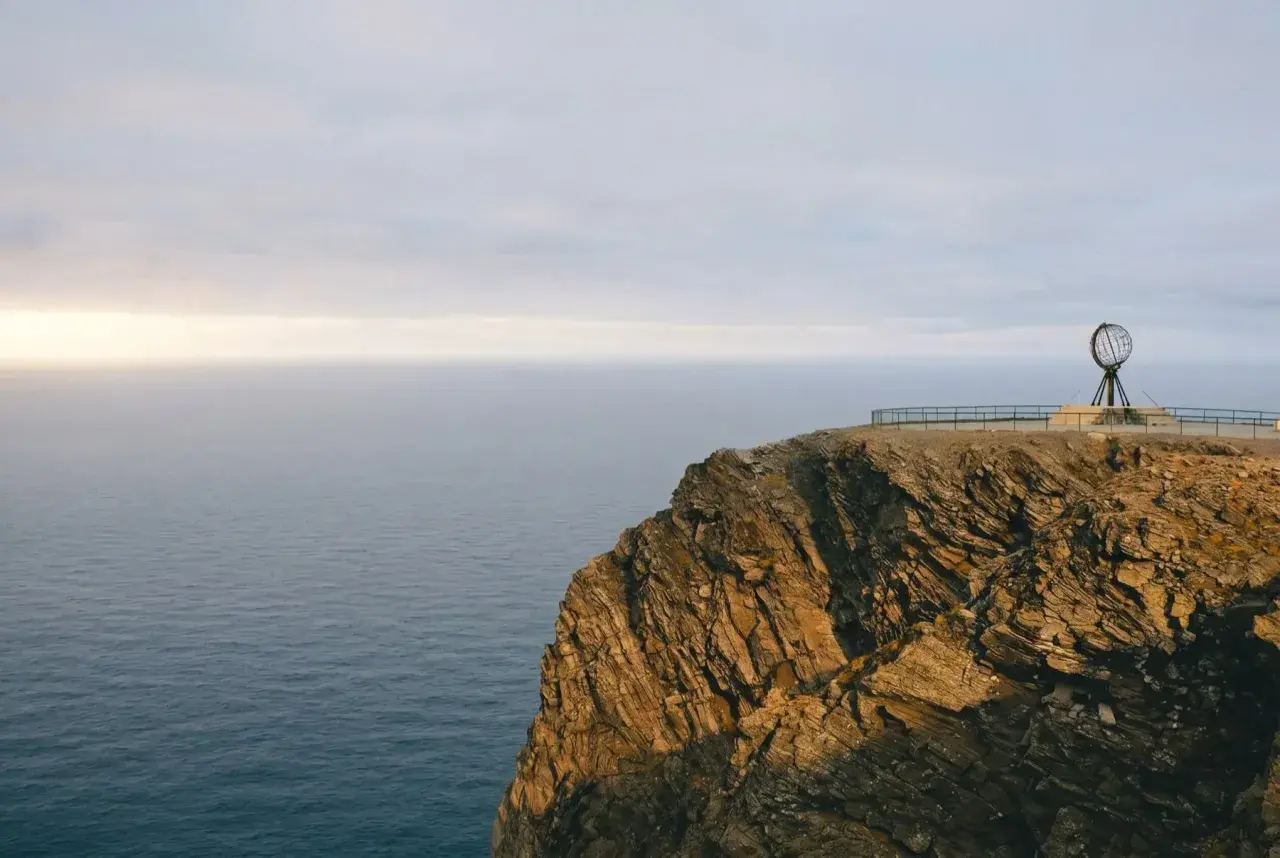Skała na Nordkapp z globusem i morzem w tle.