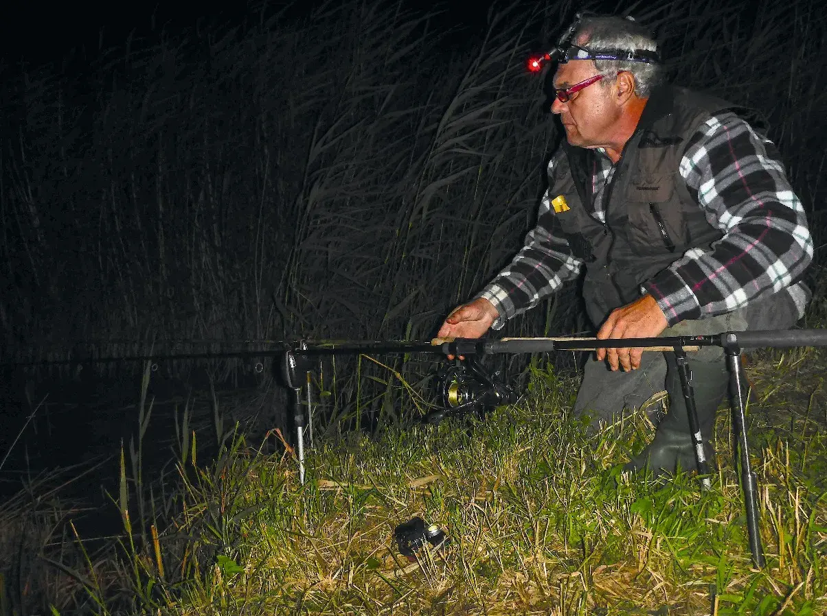 Ein Angler mit Stirnlampe prüft nachts seine John Sidley Rig-Ausrüstung am Ufer.