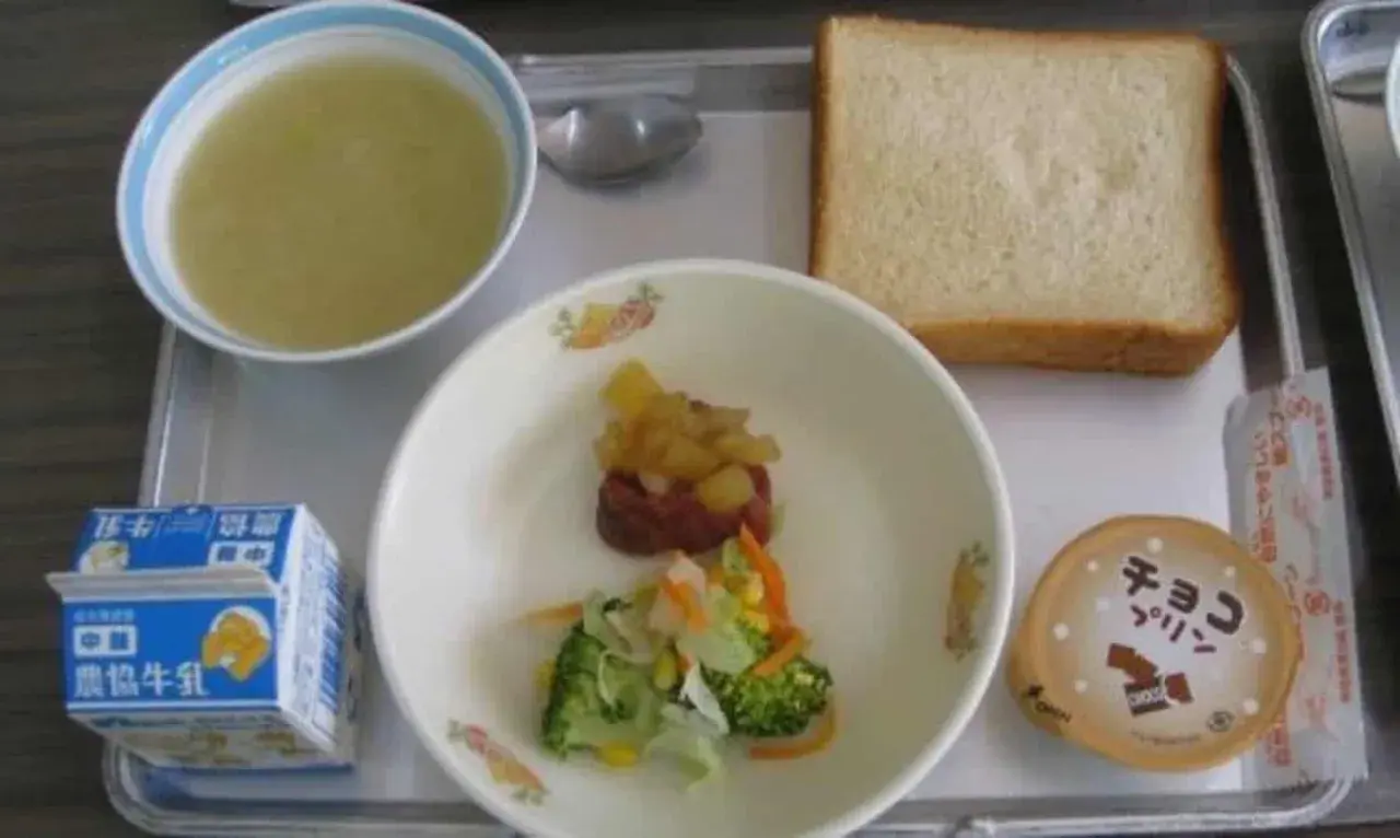 A typical Japanese school lunch tray with soup, bread, vegetables, meat, pudding, and milk.