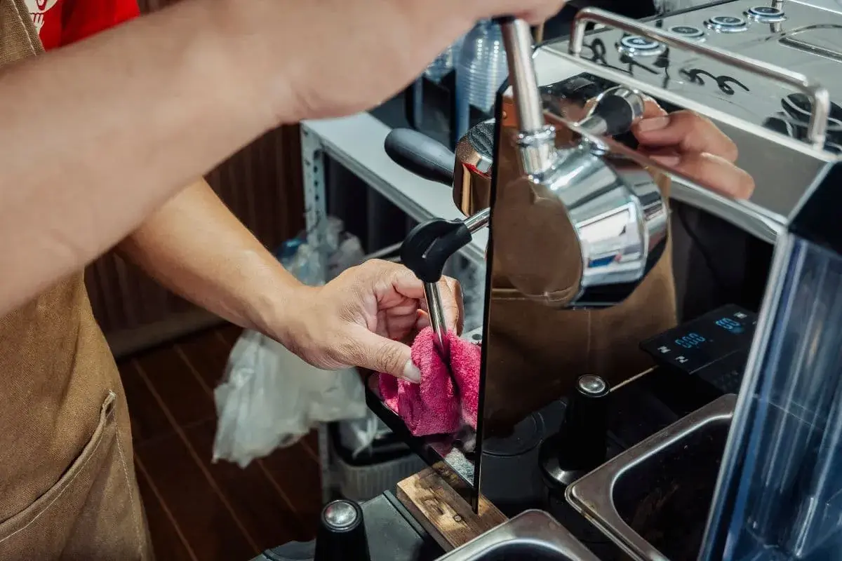 Ręce barista czyszczą dyszę ekspresu, przygotowując go do odkamieniania. Dbałość o sprzęt zapewnia idealne lattego.