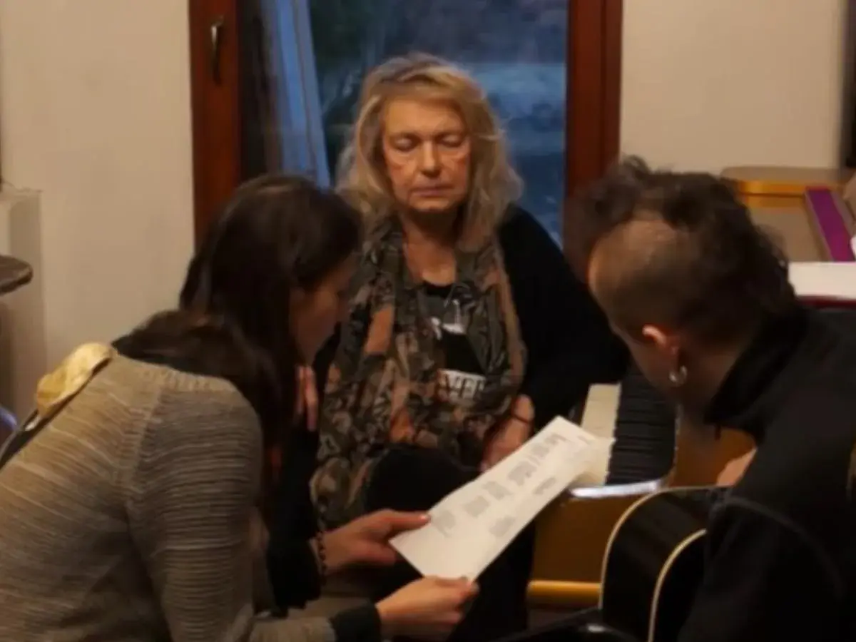 Katarzyna Gaertner z synem i młodą kobietą analizują nuty przy pianinie.