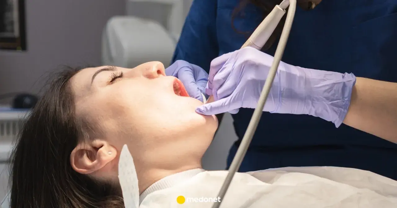 Dentysta w fioletowych rękawiczkach bada ząb pacjentki otwartymi ustami.