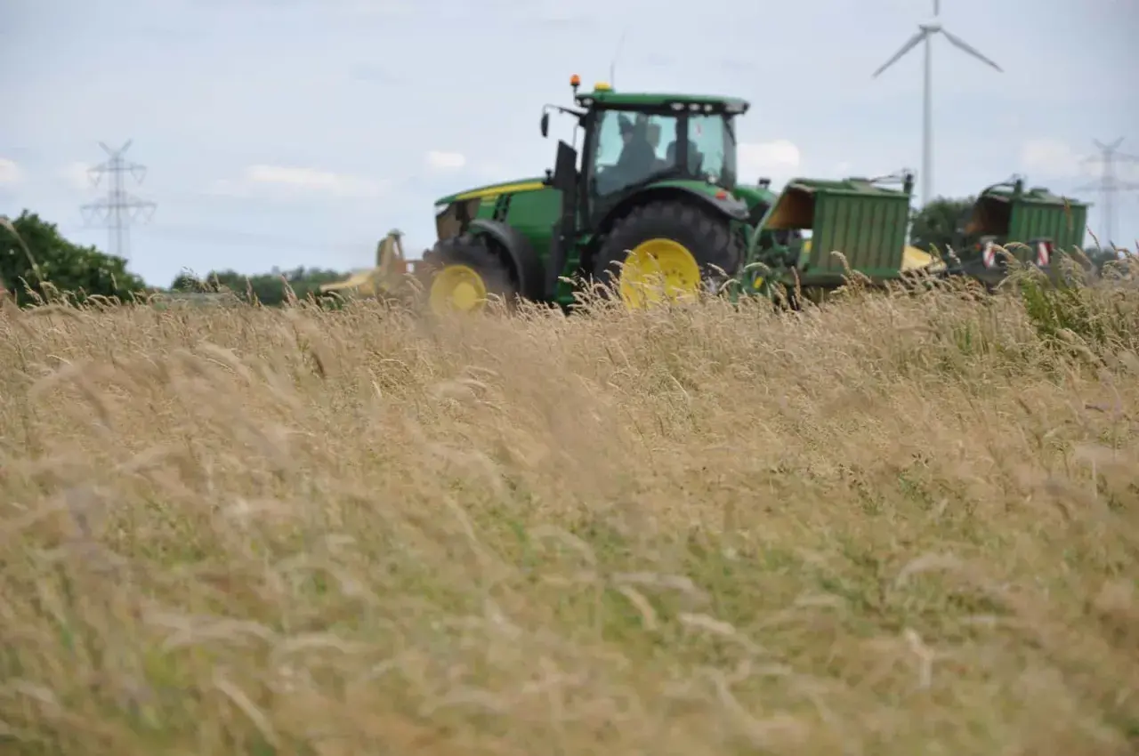 Grüner Traktor mit Anhängern im Feld, bereit für die Ernte. Die Kfz-Steuer für diesen Traktor ist ein wichtiger Faktor für Landwirte.