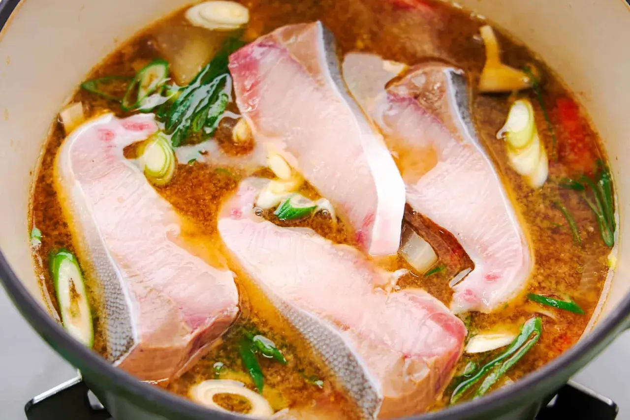 A pot of simmering Japanese fish soup with tender white fish fillets, green onions, and ginger.