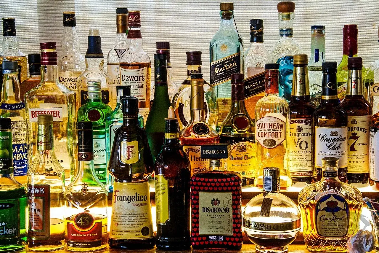 Różnorodne rodzaje alkoholi: whisky, likiery, gin, brandy i inne, stojące na półce.