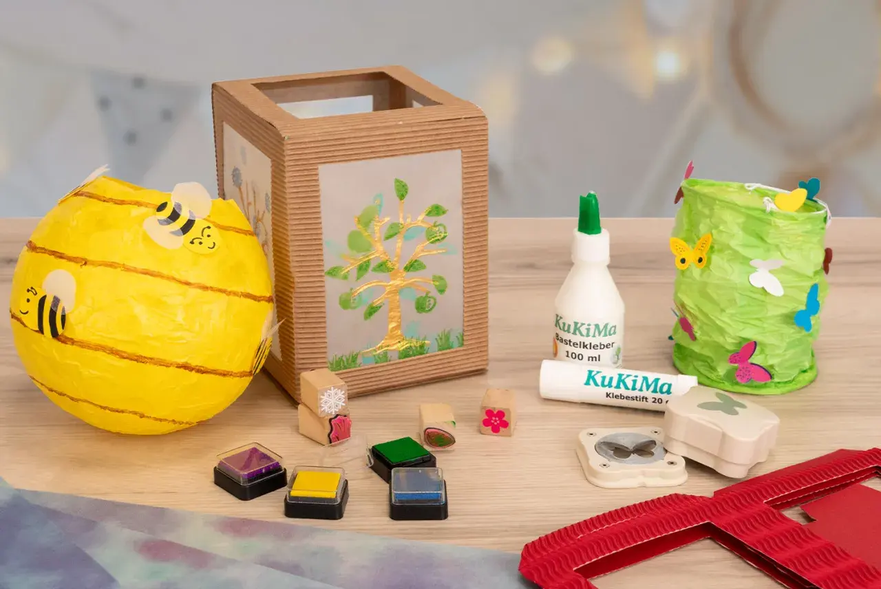 Bastelmaterialien für eine St. Martin Laterne: Bienen-Laterne, Baum-Laterne, Kleber, Stempel und Schmetterlingsstanzer.
