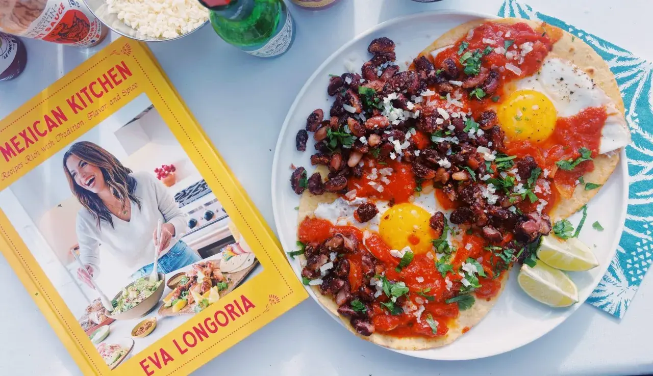 Deux œufs sur le plat, haricots noirs et sauce tomate sur tortillas, inspirés par le livre "Mexican Kitchen" d'Eva Longoria. Un plat de huevos rancheros savoureux.