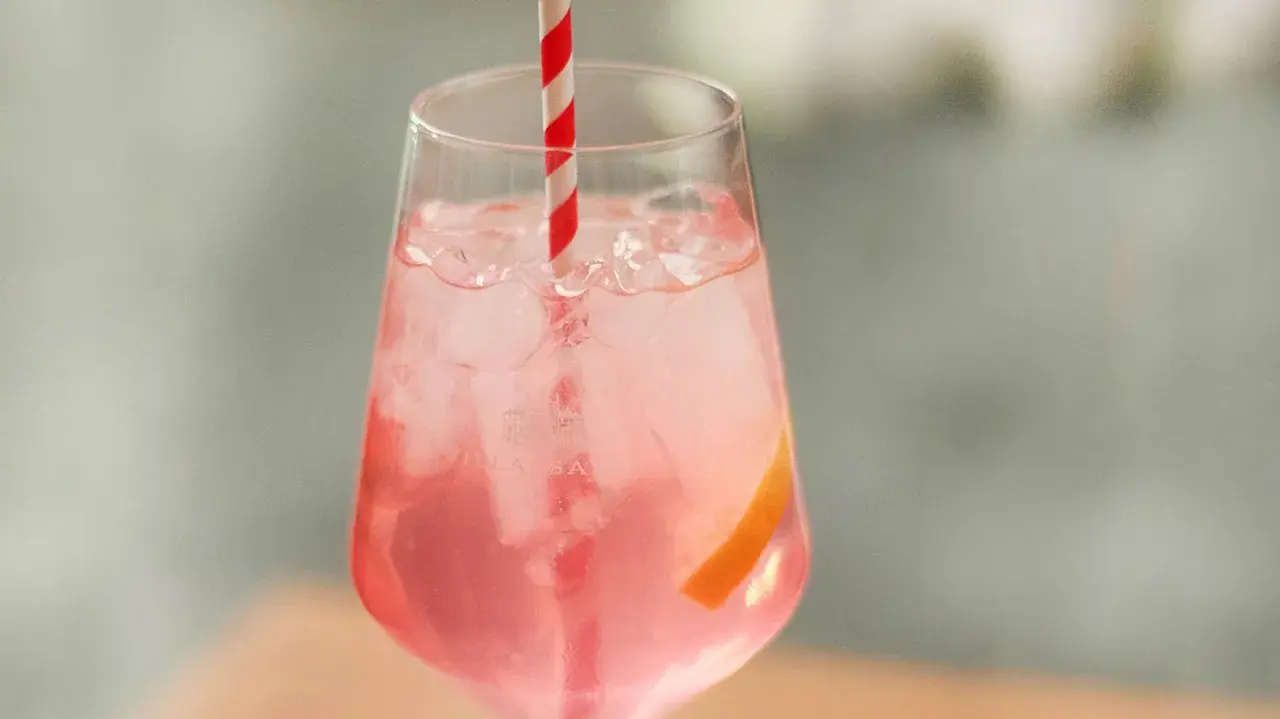 Erfrischender Sarti Spritz mit Eiswürfeln, einer Orangenscheibe und einem rot-weißen Strohhalm.