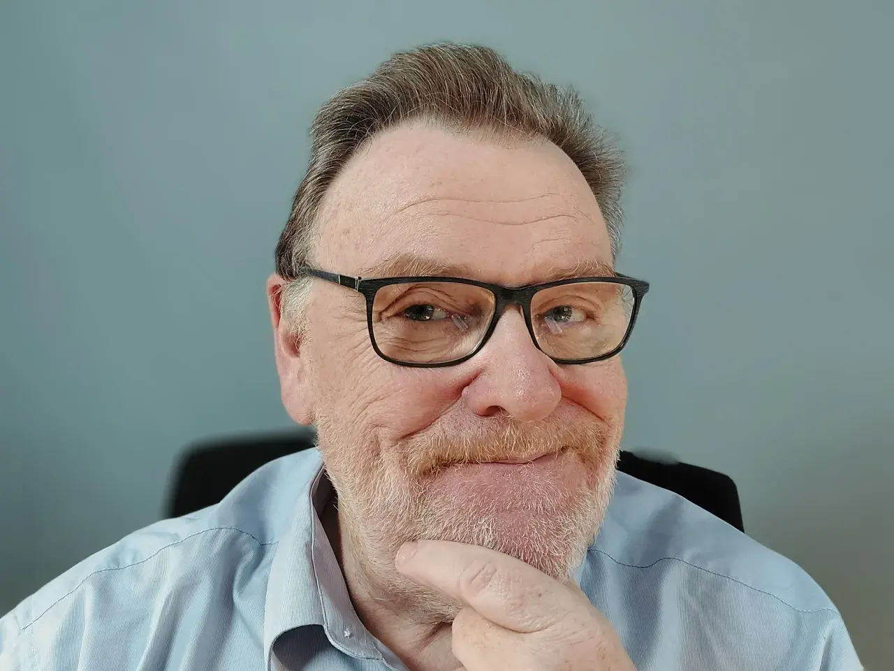 Porträt eines älteren Mannes mit Brille und Bart, der nachdenklich seinen Finger am Kinn hat.