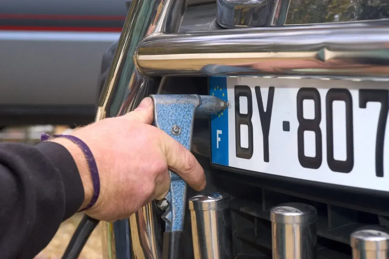 Mano con rivettatrice che fissa una targa auto, forse per cambiare targa auto per sfizio.