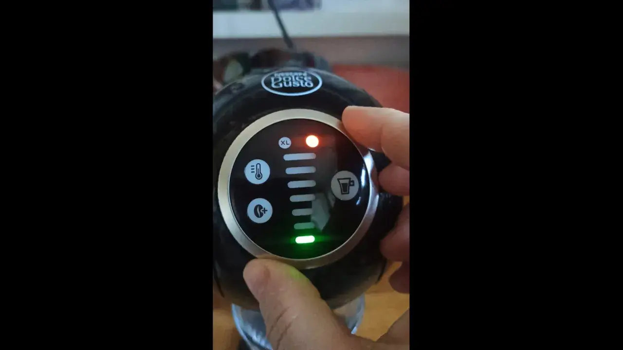 Dłoń naciska przycisk na ekspresie Dolce Gusto. Czerwona lampka sygnalizuje problem, a zielona wskazuje, że dolce gusto cieknie woda.