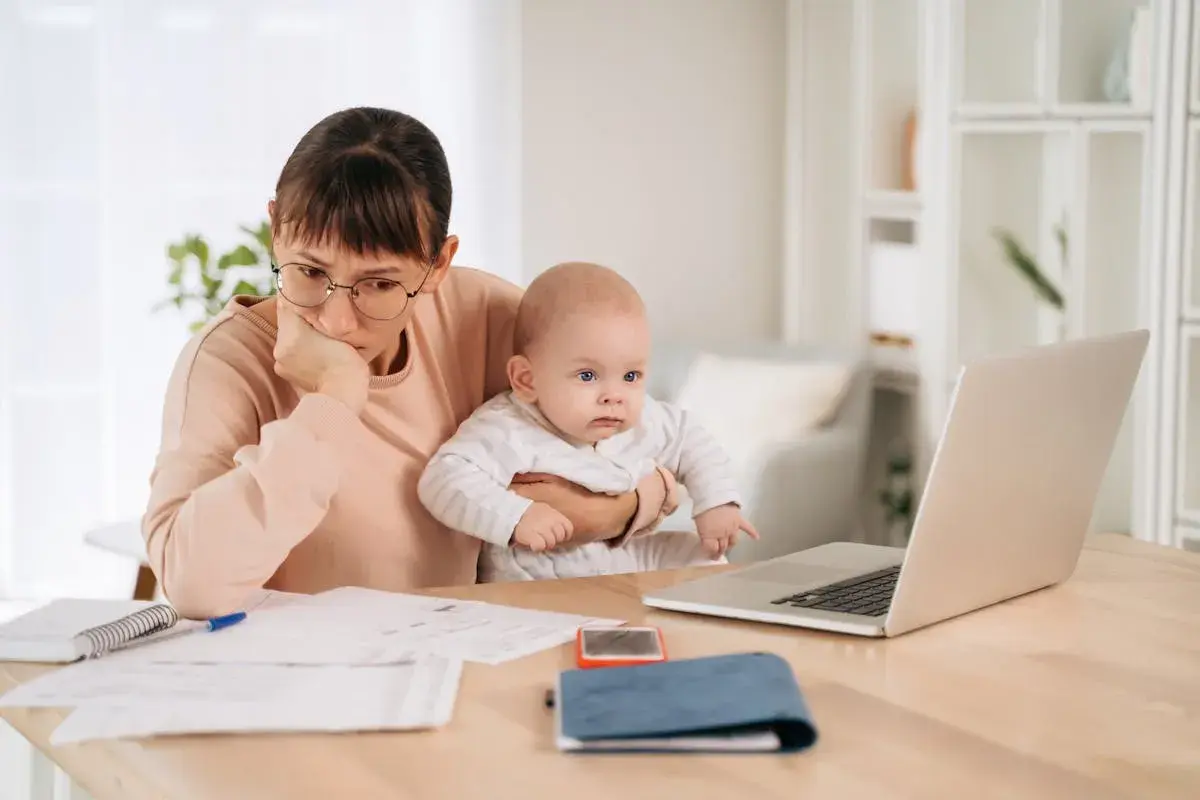 Mère pensive avec bébé, jonglant entre le travail et le renouvellement congé parental CAF.