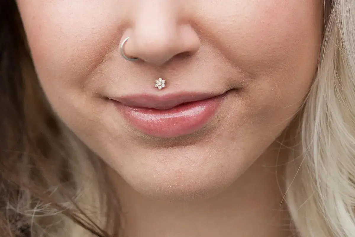 Usta z błyszczącym błyszczykiem i kwiatowym medusa piercingiem. Kolczyk w nosie dodaje uroku.