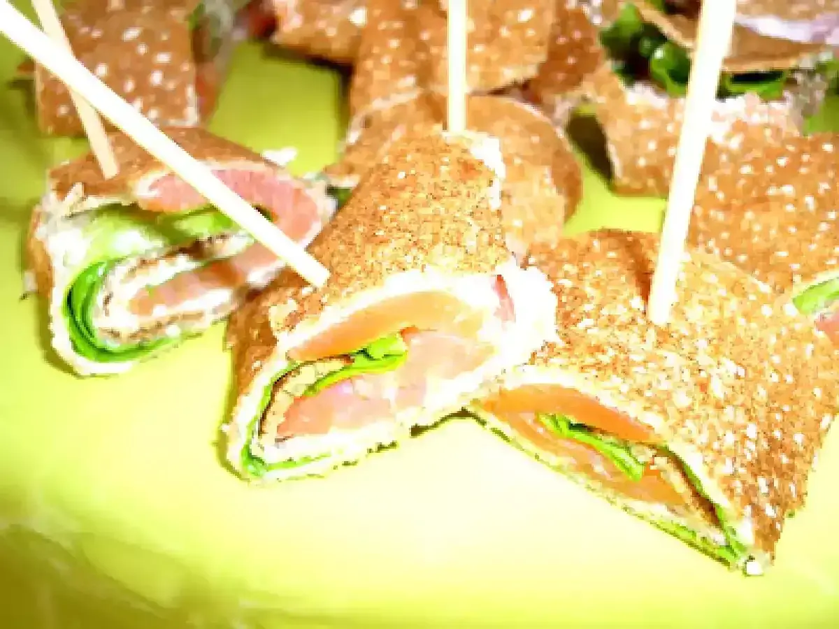 Rouleaux de galette sarrasin garnis de saumon fumé et de salade verte, servis sur une assiette jaune vif.