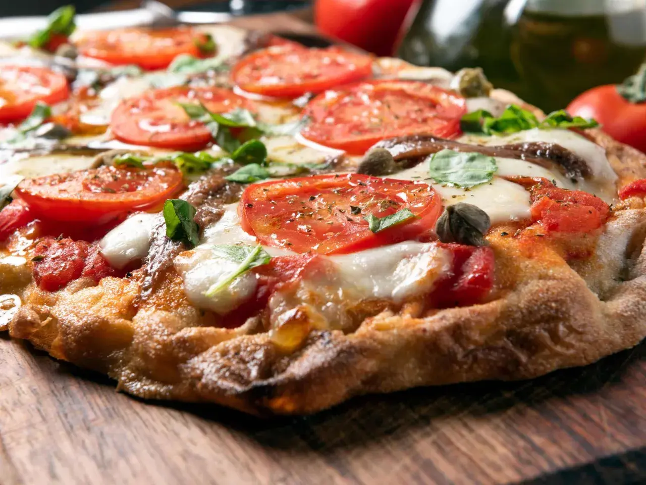 Knusprige Pizza mit Tomaten, Mozzarella und Basilikum auf einem Holzbrett.