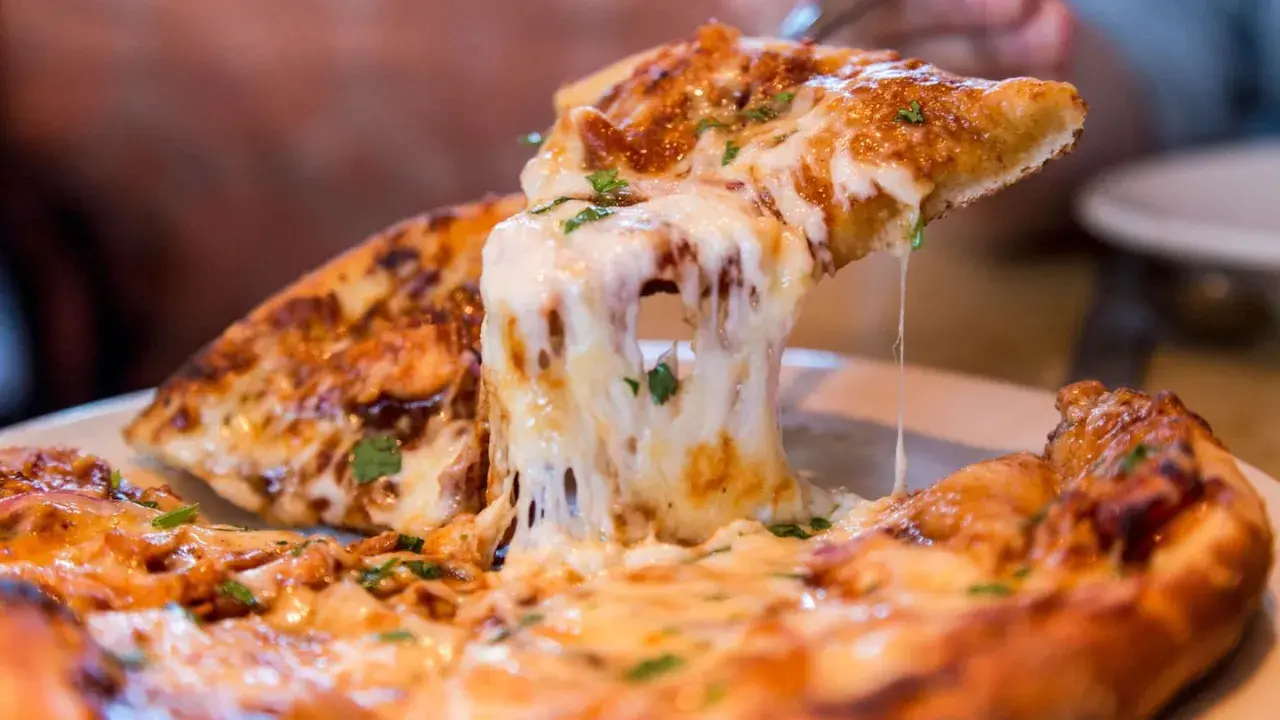 Ein Stück Pizza mit geschmolzenem Käse wird hochgehoben. Die vielen Pizza Kalorien sind es wert!