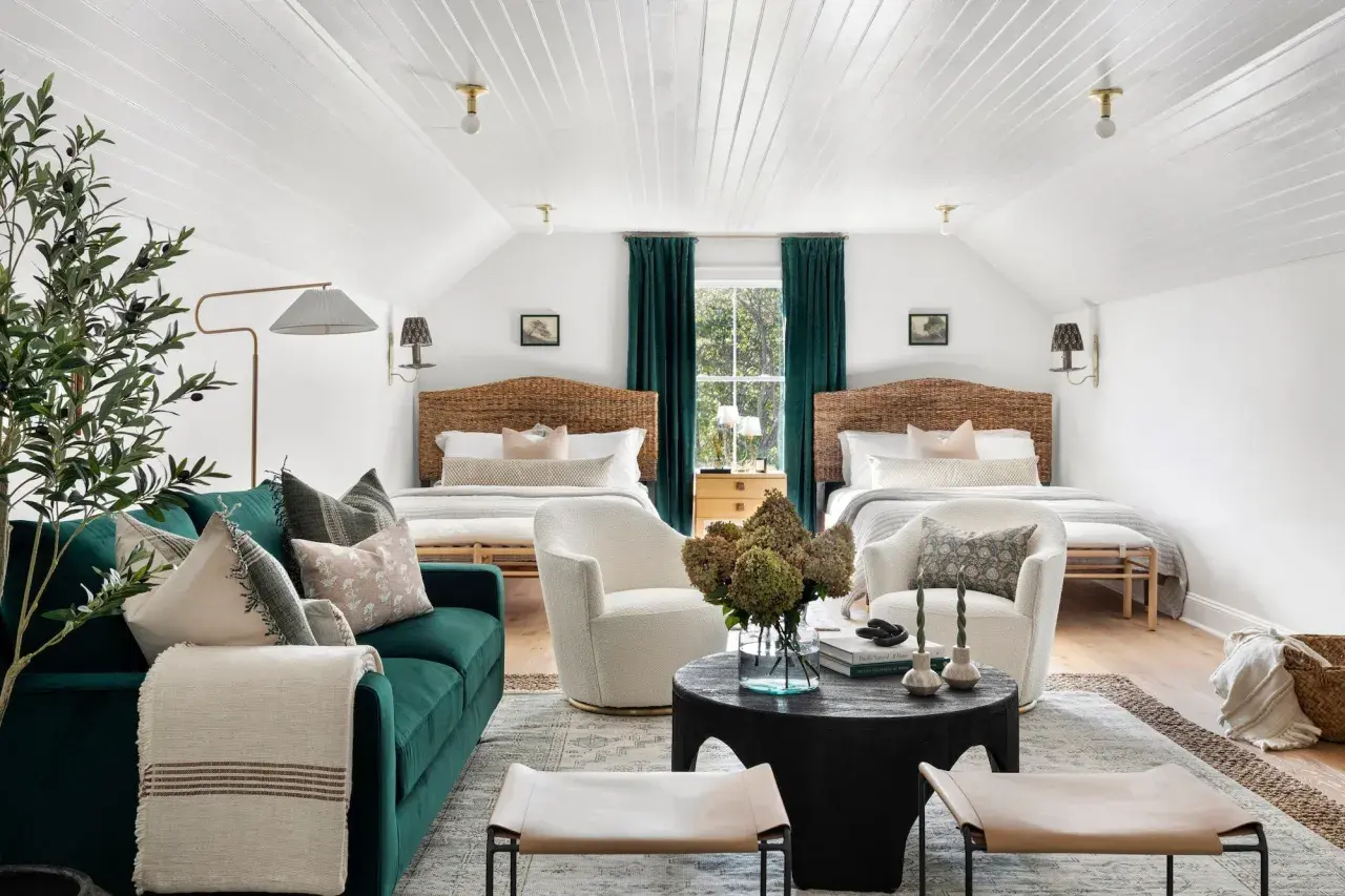 Two beds flank a window with teal curtains. Multiple rugs define the seating and sleeping areas in this cozy room.