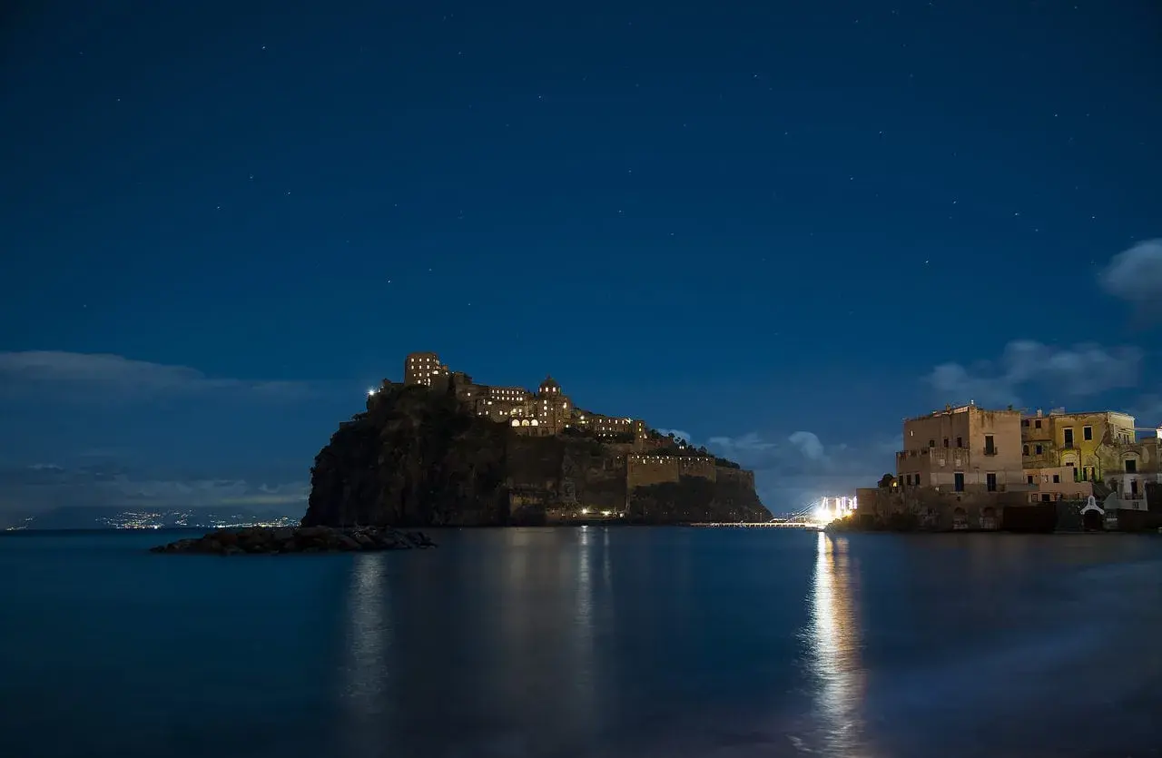 Castello Aragonese illuminato di notte, riflesso sull'acqua, sotto un cielo stellato. Un'opera di Gabriele Mattera.