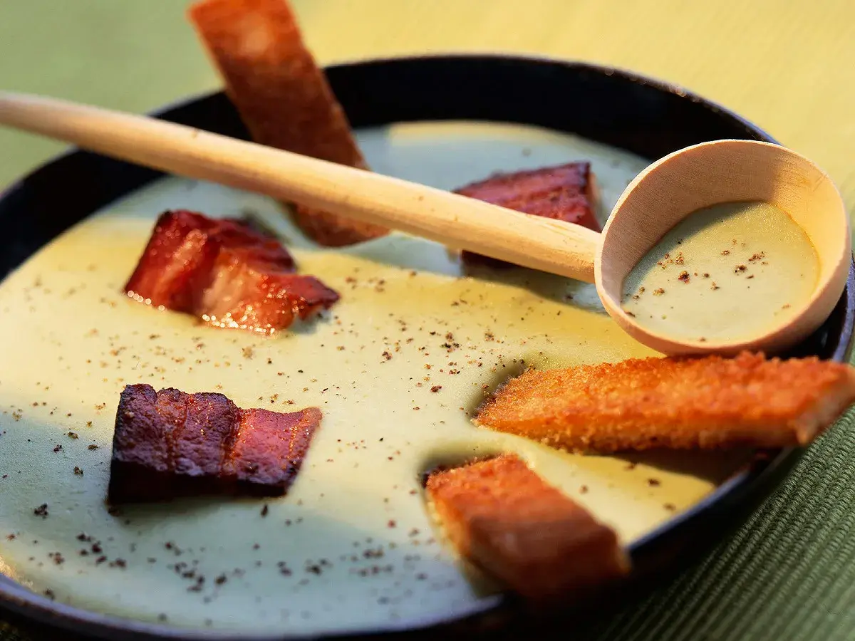 Une cuillère en bois sert une soupe de pois cassés onctueuse, garnie de lard croustillant et de croûtons dorés.
