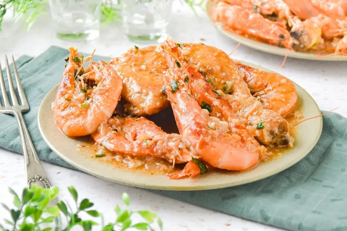Plato de pollo con gambas en salsa de ajo y perejil, servido en un plato beige con un tenedor a la izquierda.