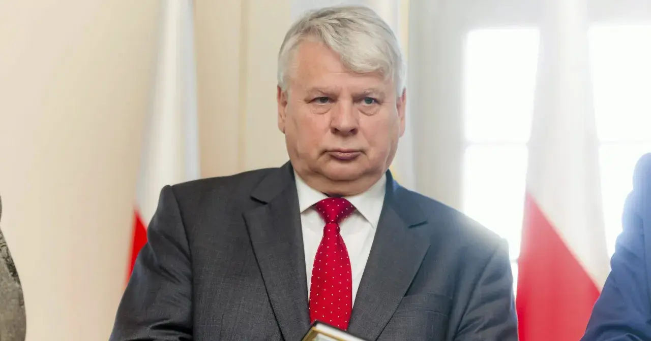 Bogdan Borusewicz w garniturze i czerwonym krawacie, na tle flagi Polski.