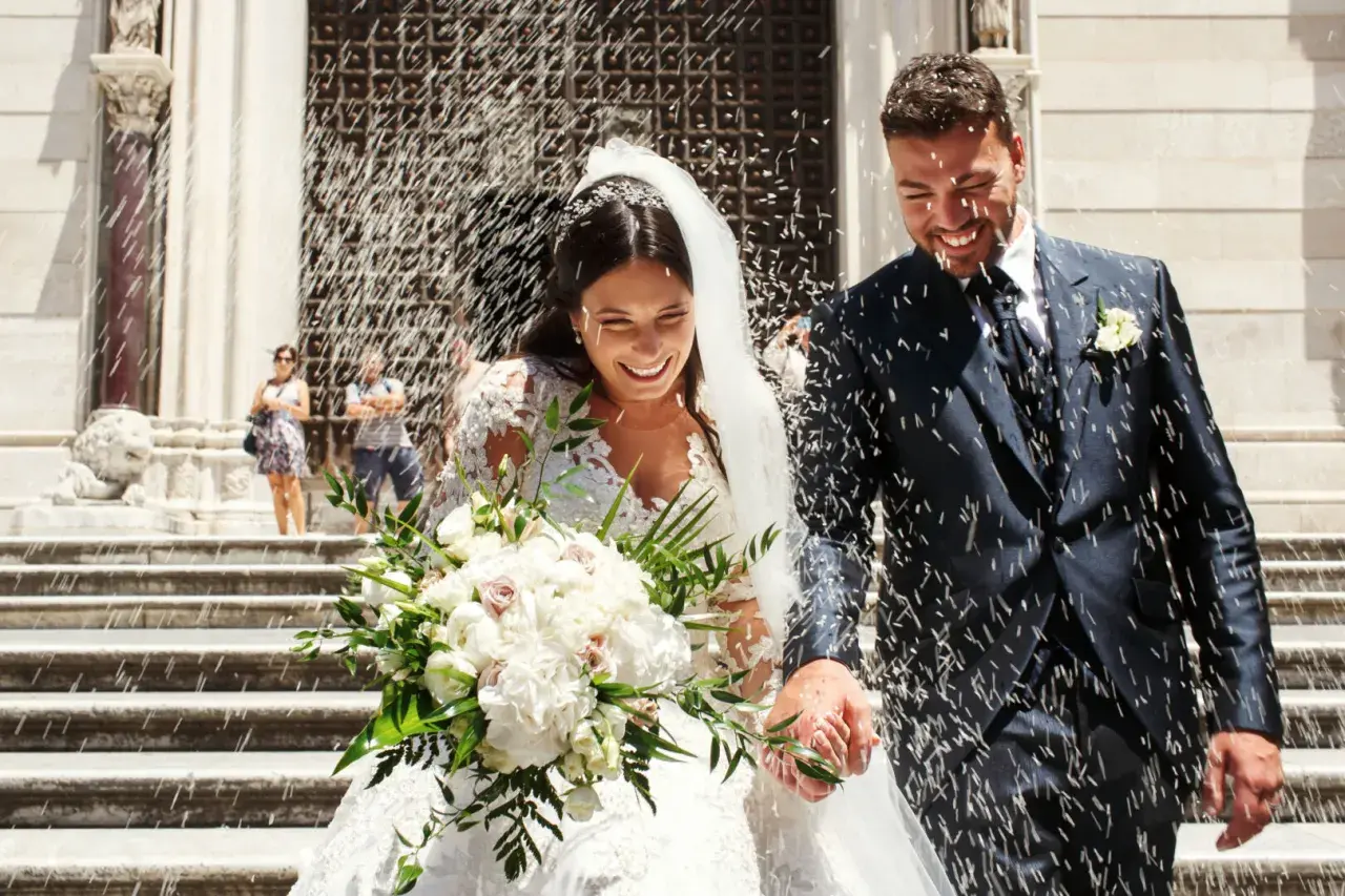 Novios felices salen de la iglesia, cubiertos de arroz. Parecen soñar con arroz, un día perfecto.