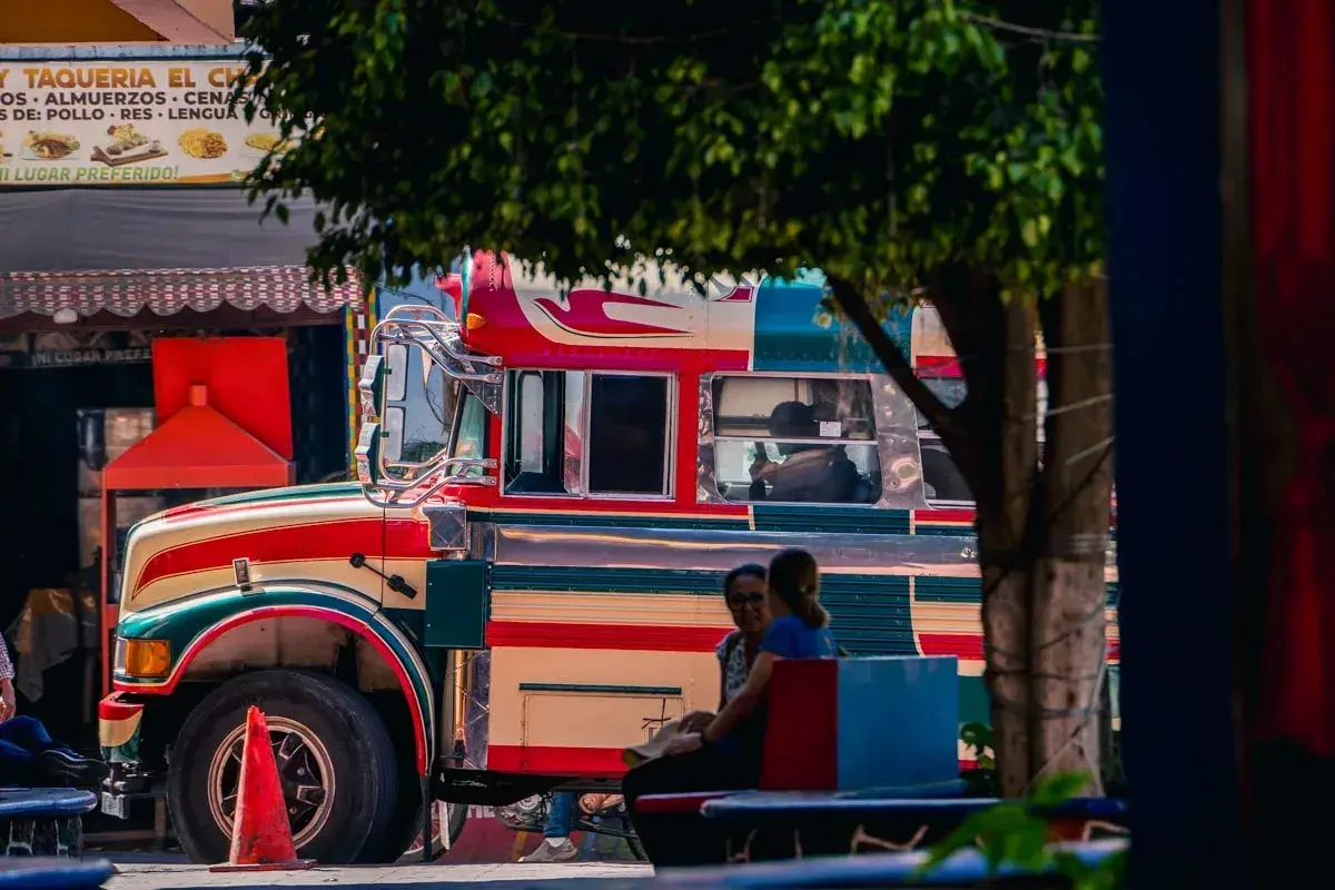 Bunter "chicken bus" in Guatemala, bereit für die nächste Fahrt. Menschen warten auf dem Bürgersteig.