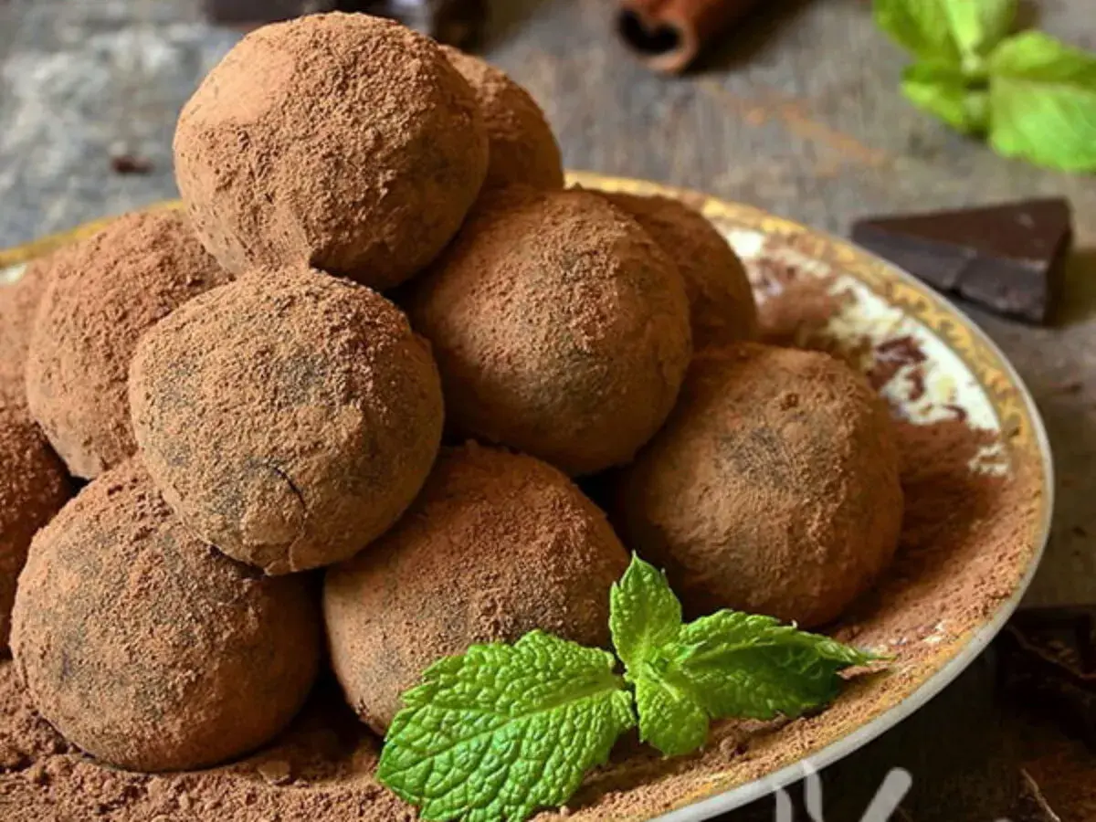 Un mucchio di tartufi al cioccolato facili e veloci, spolverati di cacao, su un piatto decorato, con menta fresca e un pezzetto di cioccolato fondente.