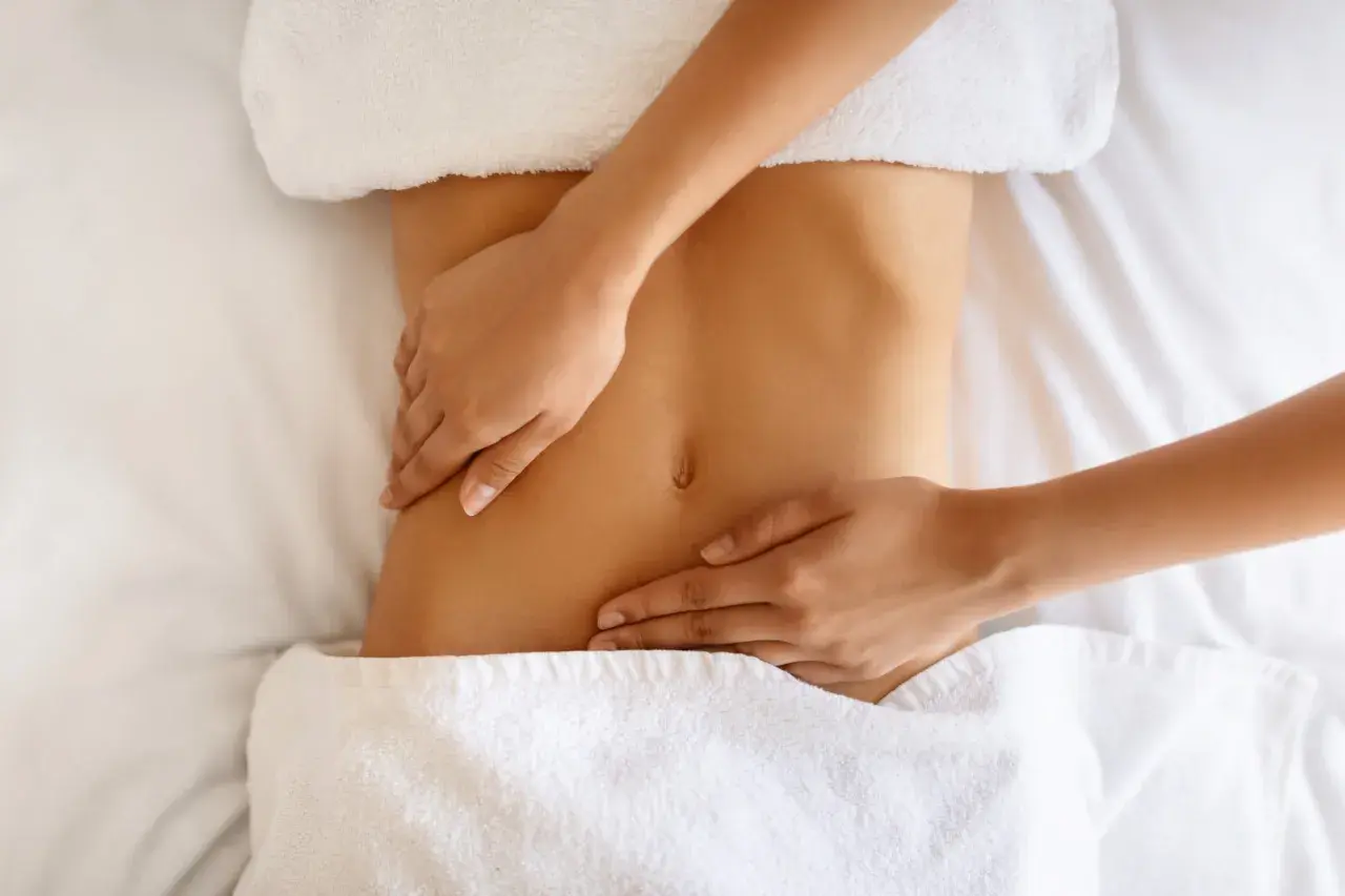 Hände massieren sanft den Bauch einer Frau. Manche empfinden Lymphdrainage als schmerzhaft, doch hier scheint es eine wohltuende Behandlung zu sein.