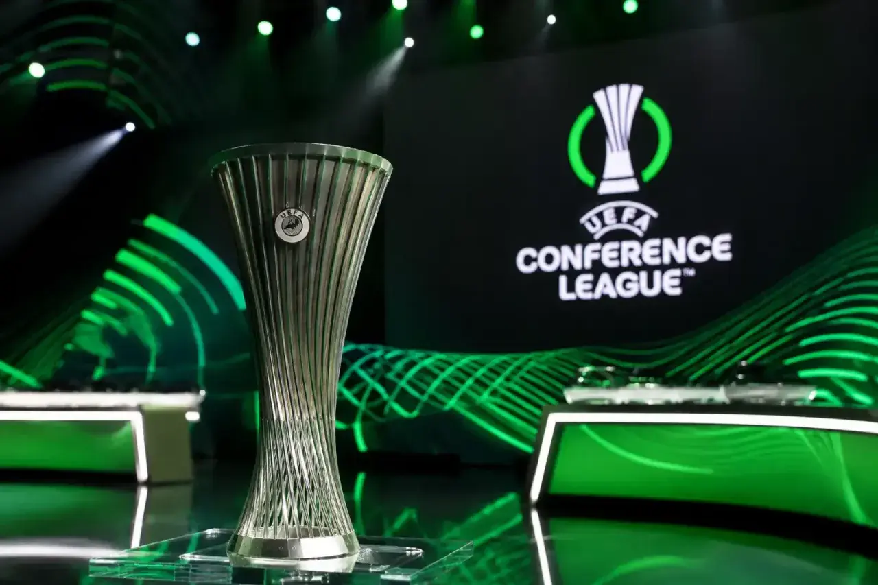 Trofeum Ligi Konferencji UEFA na tle logo i zielonych świateł. Marzenie o wygraniu tych rozgrywek napędza emocje podczas meczów ligi konferencji.