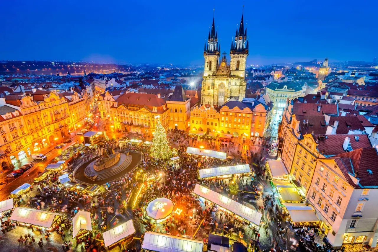 Tłoczny jarmark bożonarodzeniowy w Pradze, z oświetloną choinką i zabytkową architekturą w tle.