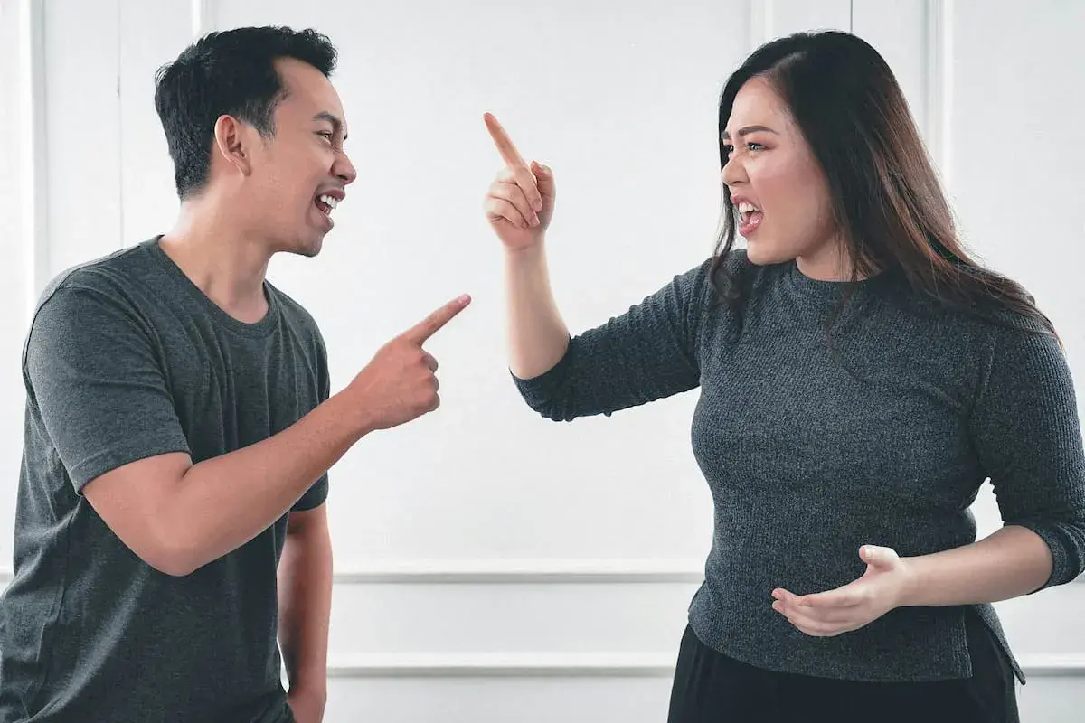 Pareja discutiendo, él señala acusadoramente, ella levanta el dedo en señal de enfado. Parece que están a punto de soñar que discuten con alguien.