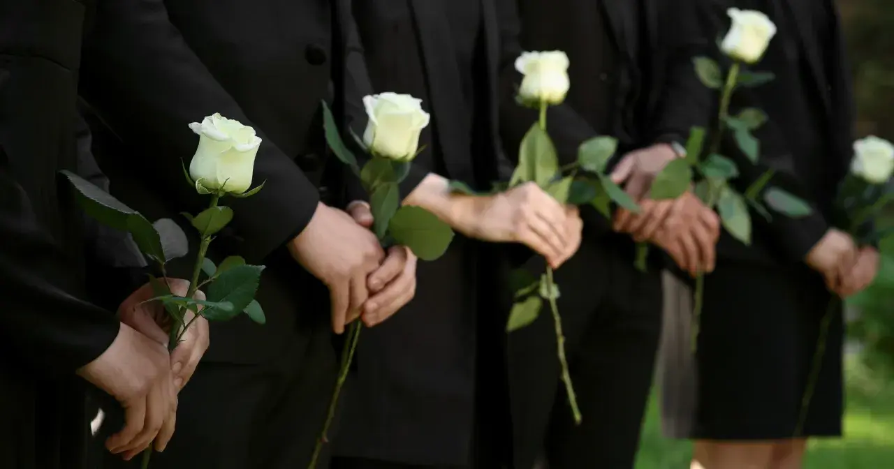 Ludzie w czerni trzymają białe róże. Mogą symbolizować żałobę, ale też nadzieję, która bywa trudna dla osób wierzących, gdy pojawiają się przyczyny lęku przed śmiercią.