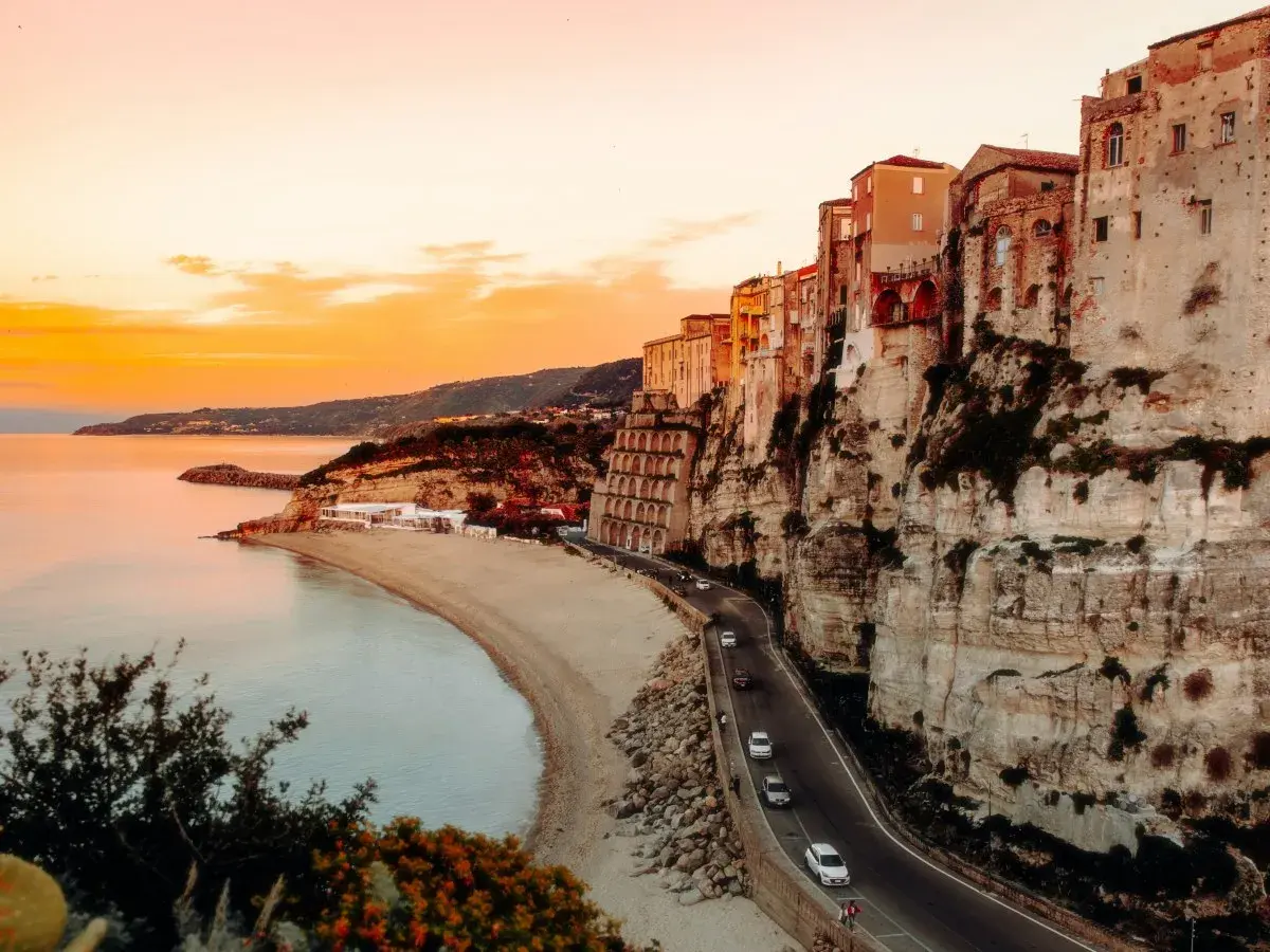 Tramonto mozzafiato sulla costa, con case aggrappate alla scogliera. Un sogno di **Calabria in moto**.