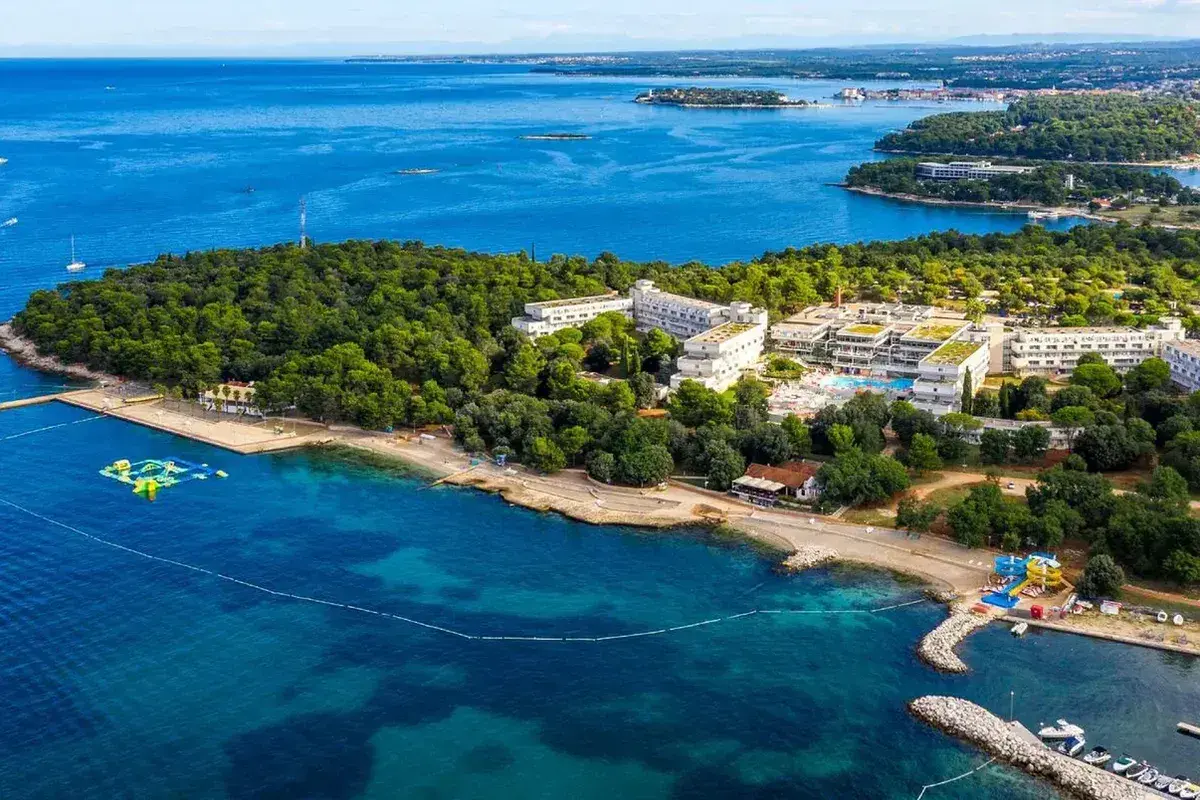 Hotel Delfin Plava Laguna, otoczony zielenią, z basenami i plażą nad turkusowym morzem.