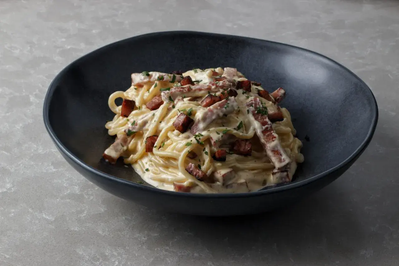 Un plat de spaghetti crémeux, garni de morceaux de guanciale croustillant et de persil frais. La vraie recette carbonara italienne, un délice simple et authentique.