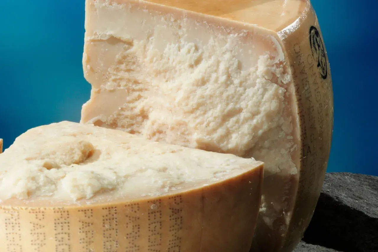 Due pezzi di Parmigiano Reggiano, uno tagliato, mostrano la loro consistenza granulosa. Scopri come conservare il parmigiano in frigo per mantenerlo fresco.