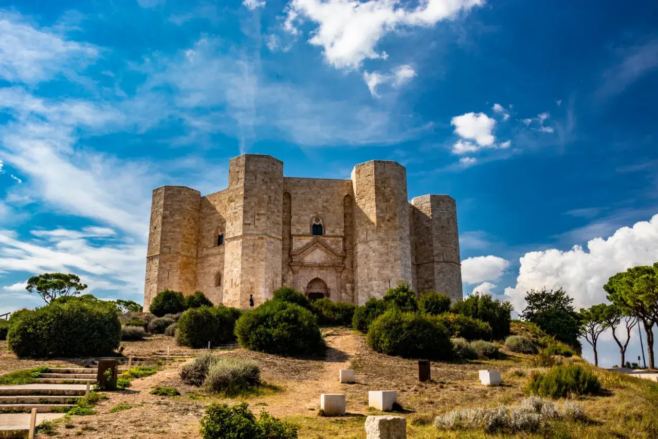 Castel del Monte, un'imponente fortezza ottagonale, si erge su una collina sotto un cielo azzurro e nuvoloso. Un luogo perfetto per chi ama visitare Castel del Monte.