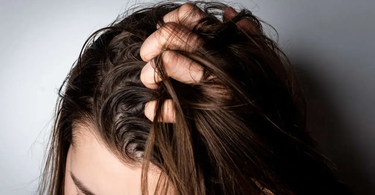 Mano revolviendo cabello oscuro y lacio. ¿Es mejor teñirse con el pelo sucio o limpio?