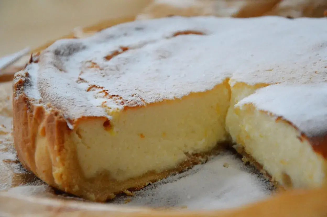 Une part de tarte à la ricotta sucrée, saupoudrée de sucre glace, révèle sa garniture crémeuse et sa croûte dorée. Un délice !