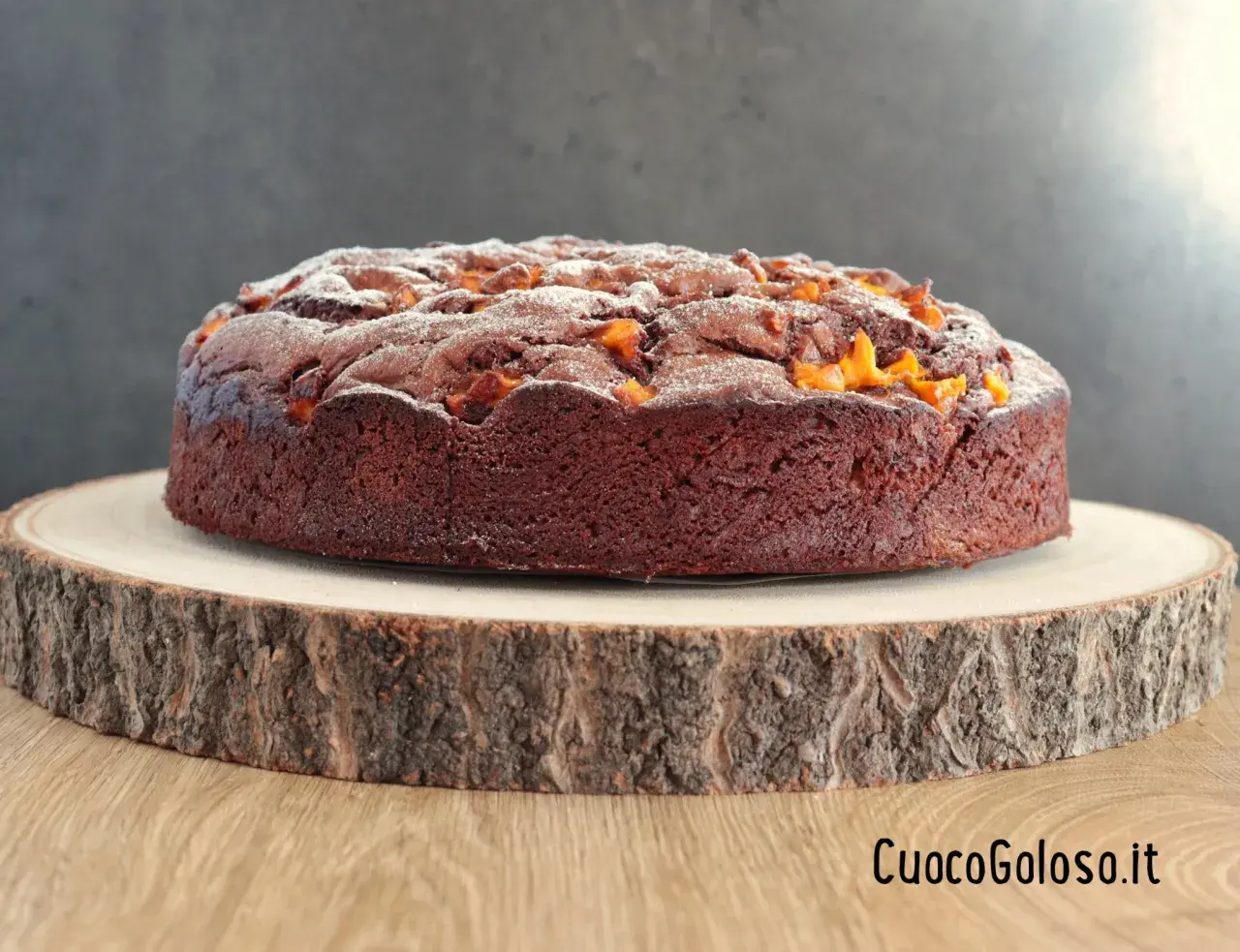 Torta al cioccolato con pezzi di mango, spolverata di zucchero a velo, su un tagliere di legno grezzo.