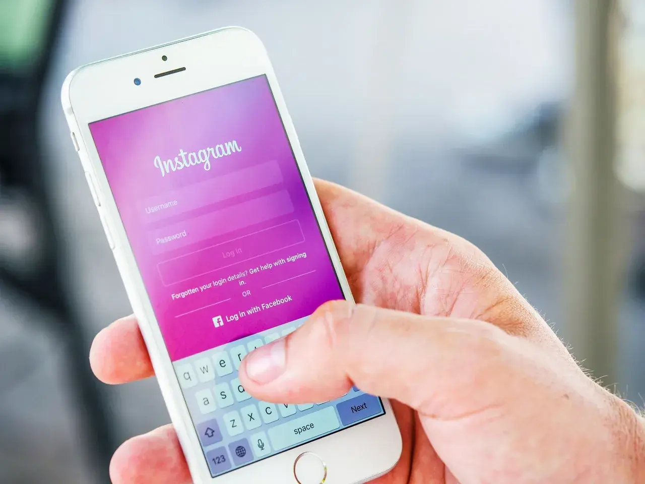 Dłoń trzyma smartfon z ekranem logowania Instagram. Widoczna opcja "Zapomniane dane logowania?" podpowiada, jak odzyskać hasło na Instagramie.