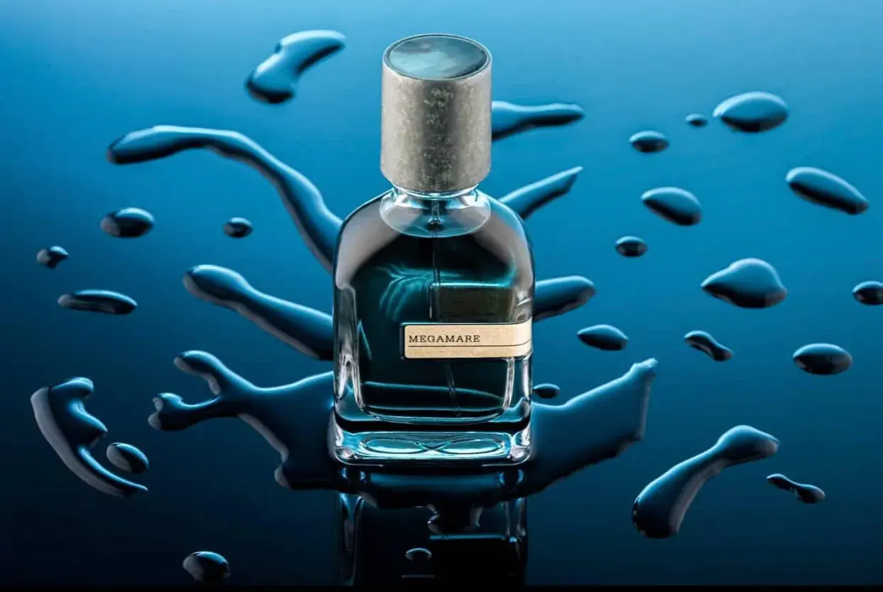Szklana butelka perfum Megamare otoczona kroplami wody na granatowym tle.