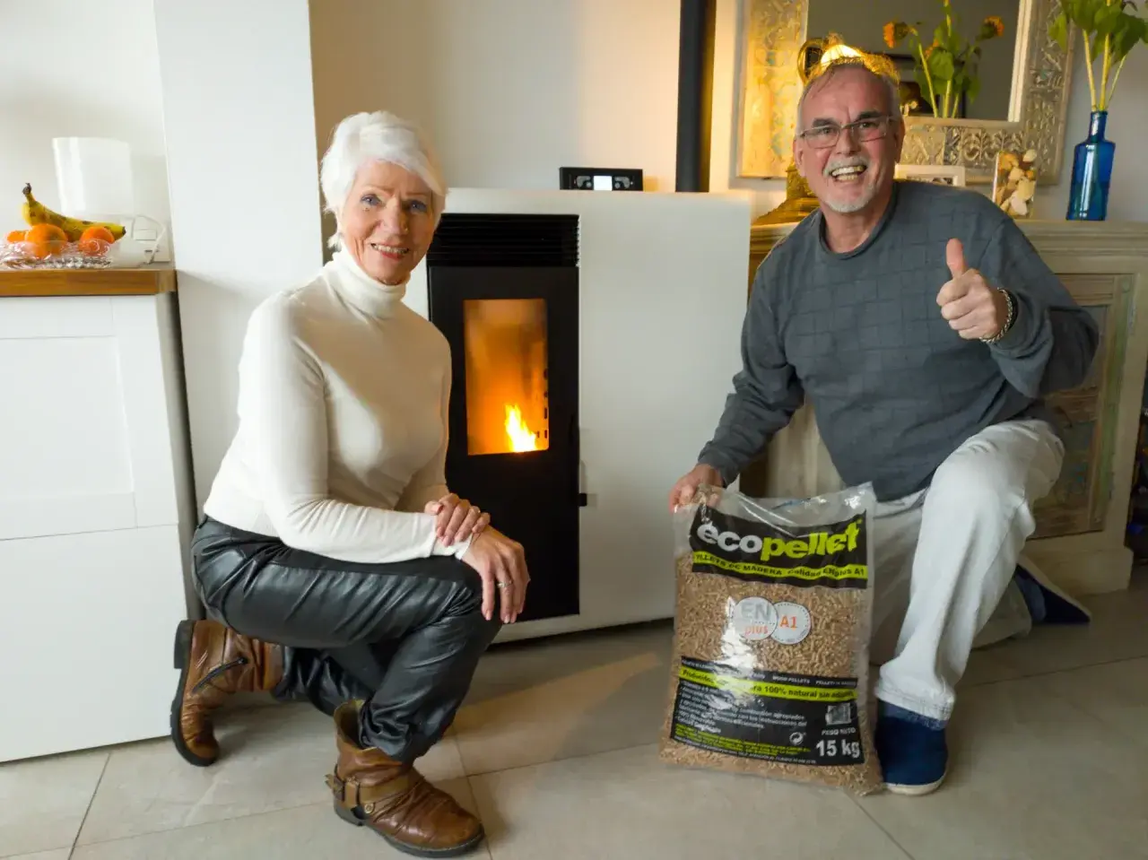 Pareja feliz junto a su nueva estufa de pellets, con una bolsa de combustible lista para la instalación.