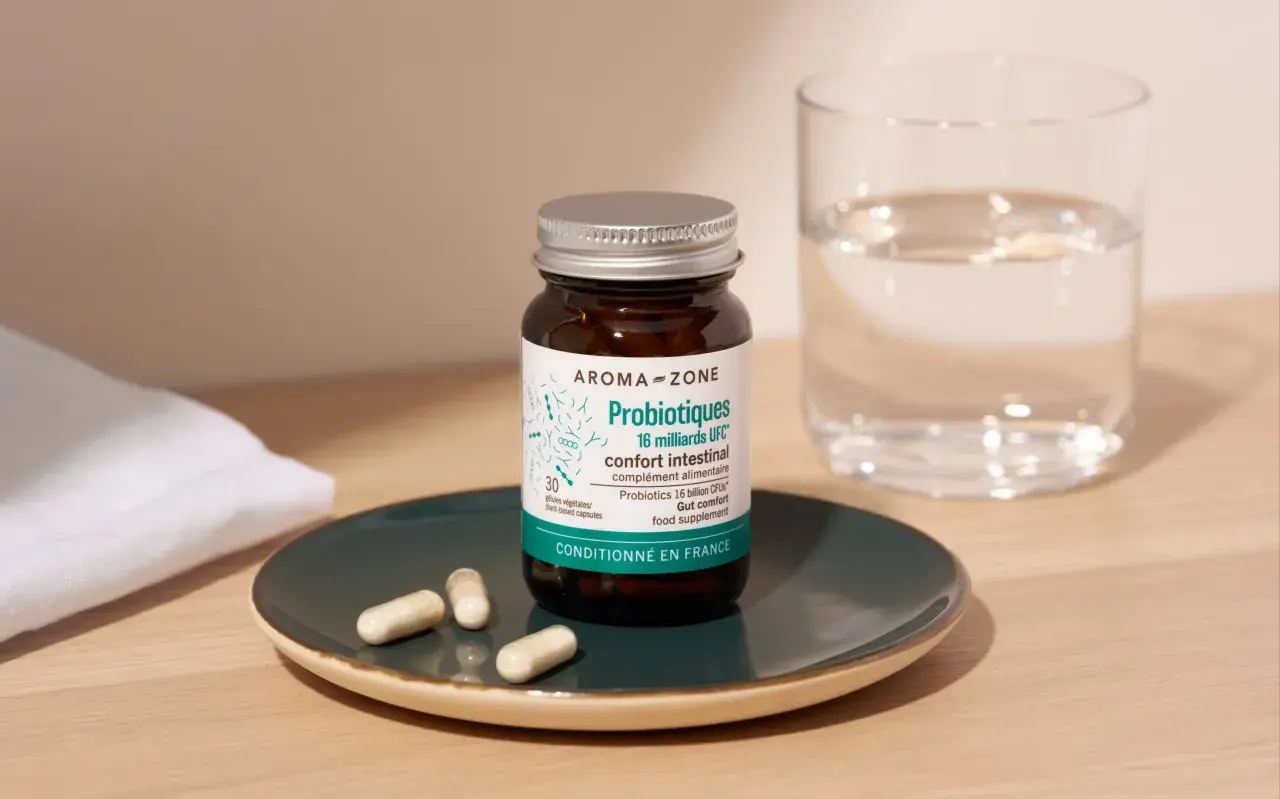 Bouteille de probiotiques Aroma-Zone sur une assiette avec des gélules, à côté d'un verre d'eau. Une cure probiotique pour le confort intestinal.