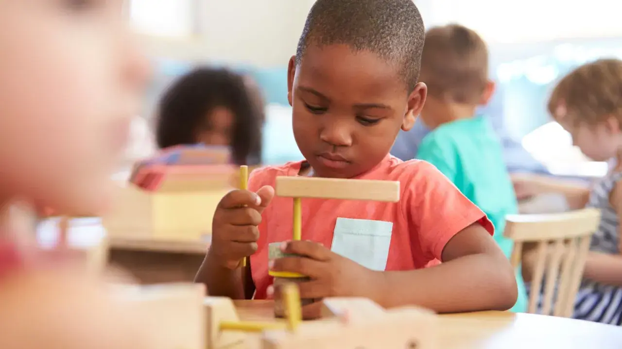 Ein Junge in einer Montessori-Schule baut konzentriert mit Holzbausteinen. So lernt man hier spielerisch.